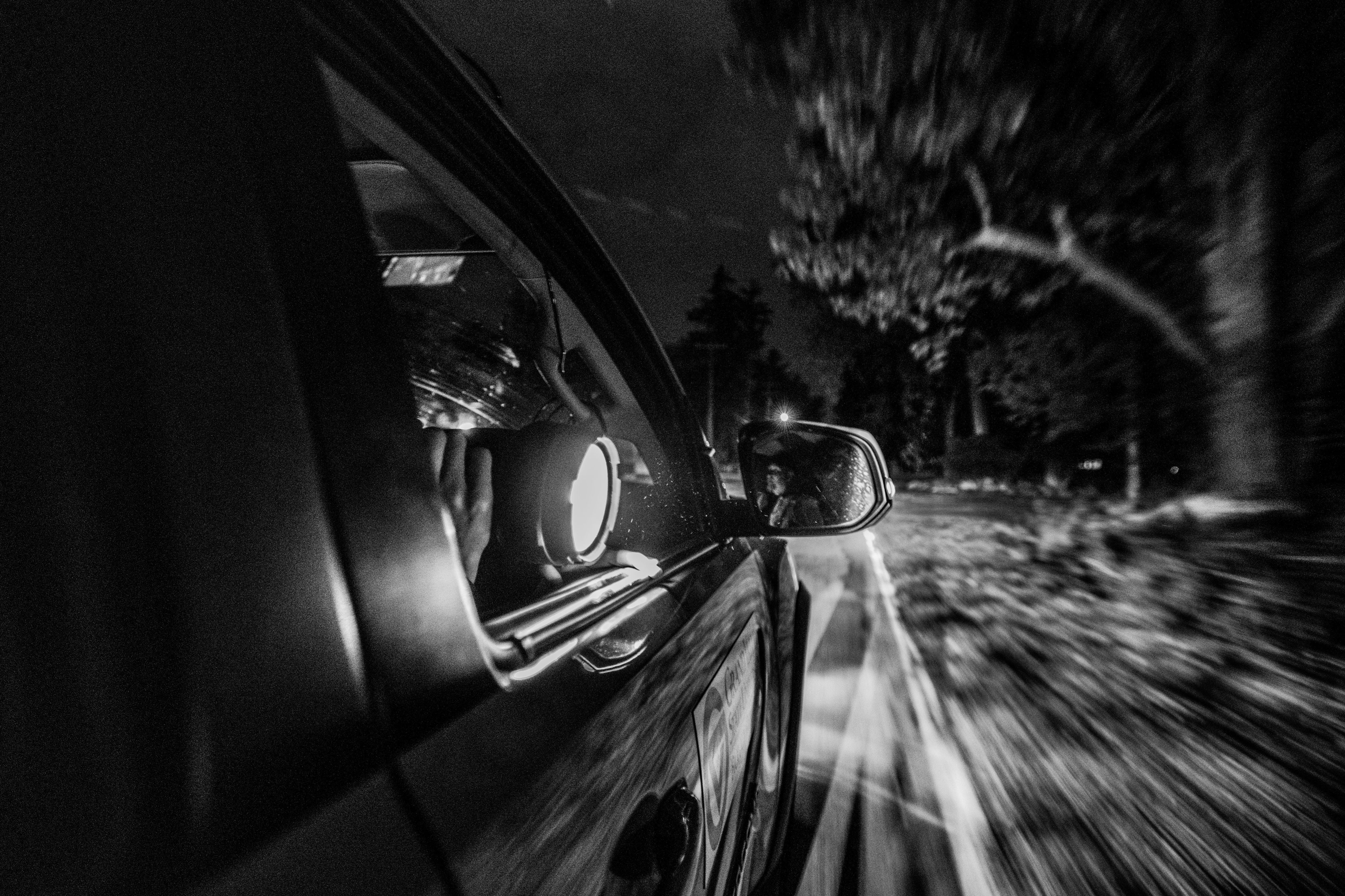 Black and white photo of a person shining a flashlight out of the passenger side window.
