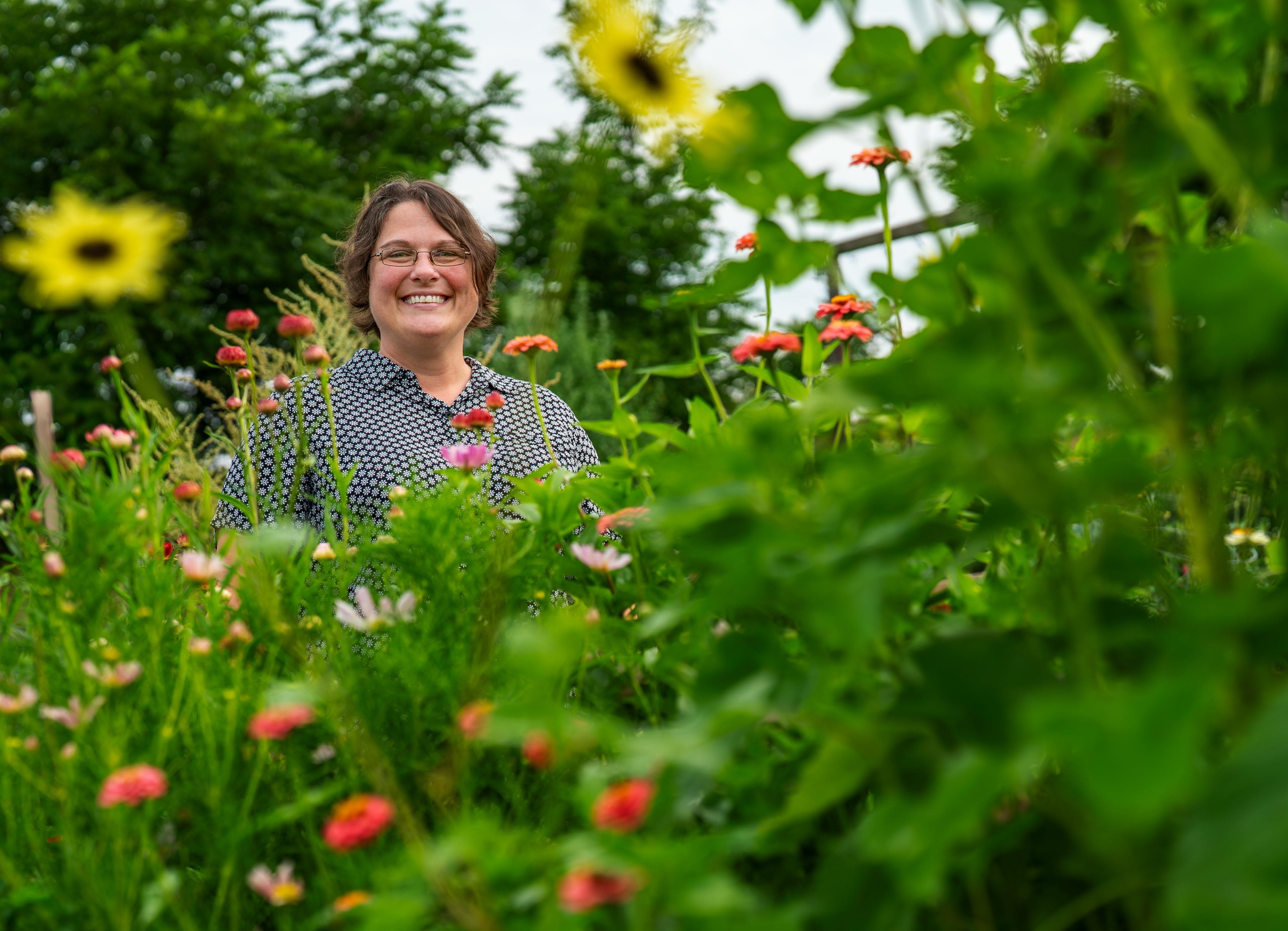 A person smiles while standing in a field of brightly covered flowers.