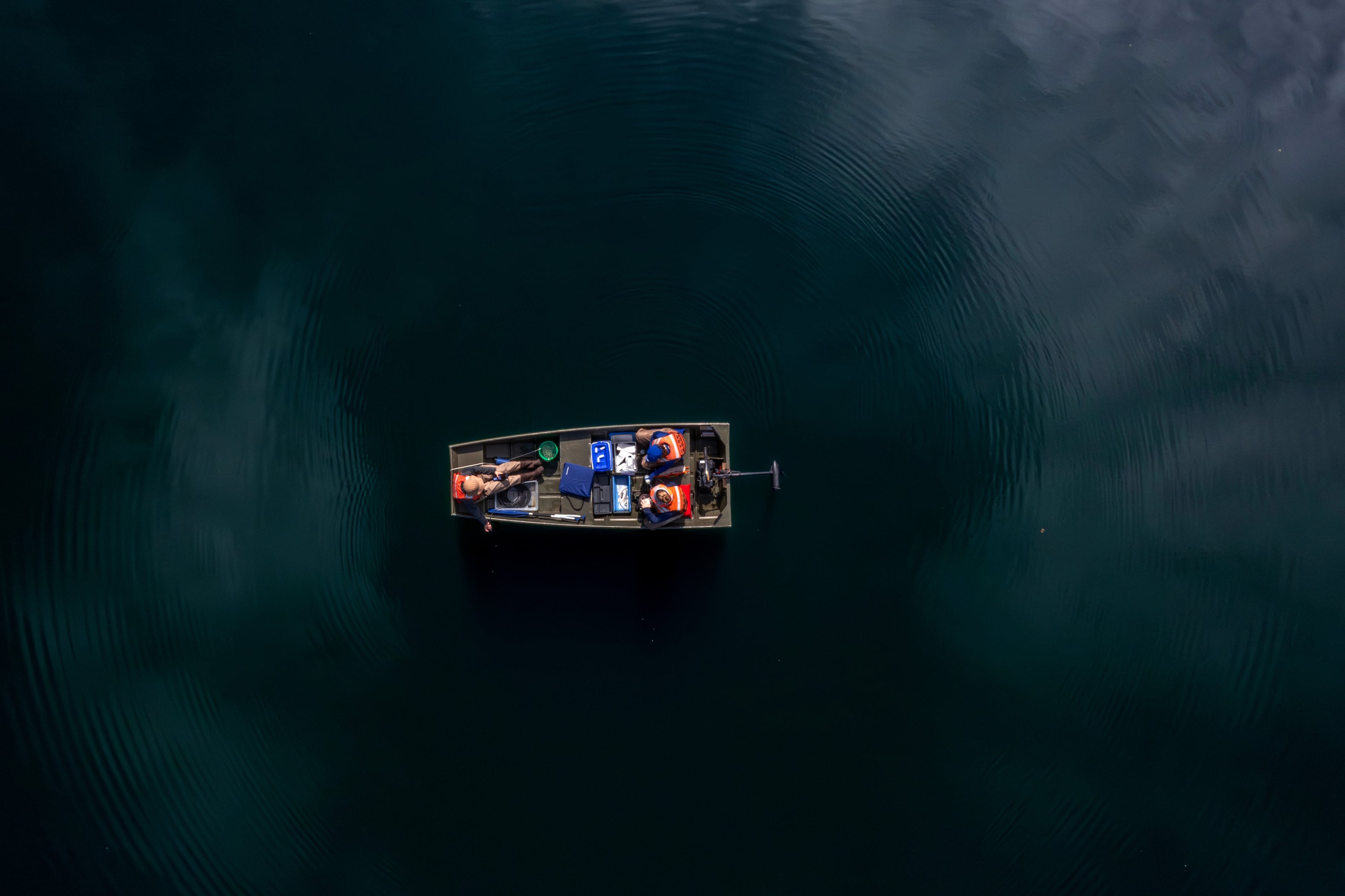Aerial view of people with life vests and supplies sitting in a boat on a lake.