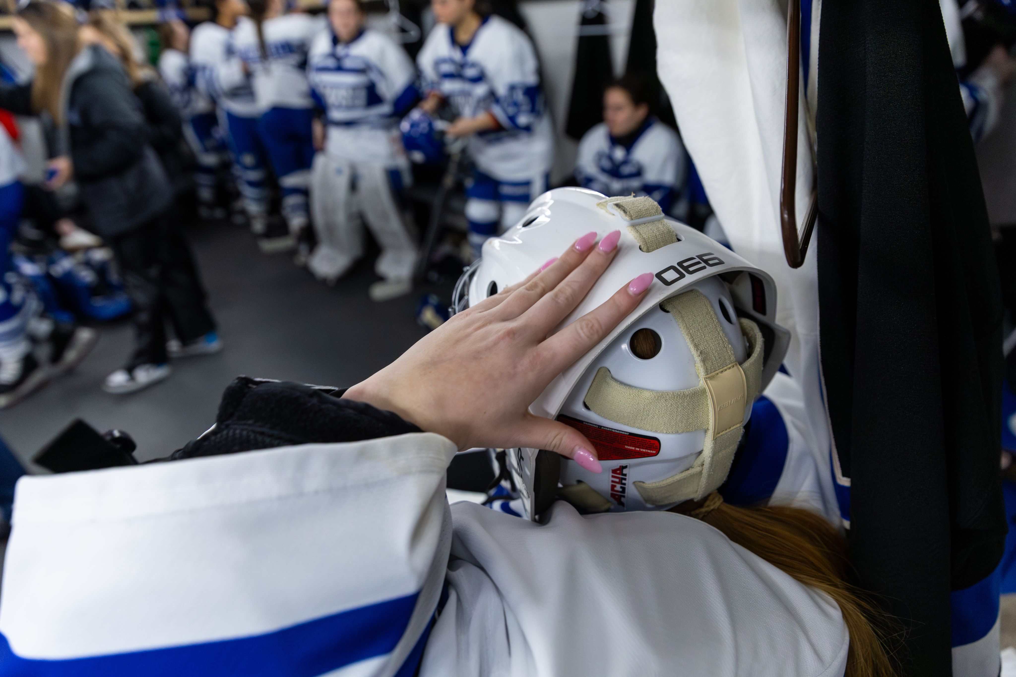 A close-up view of a hand with pink nails touching a goalie helmet.
