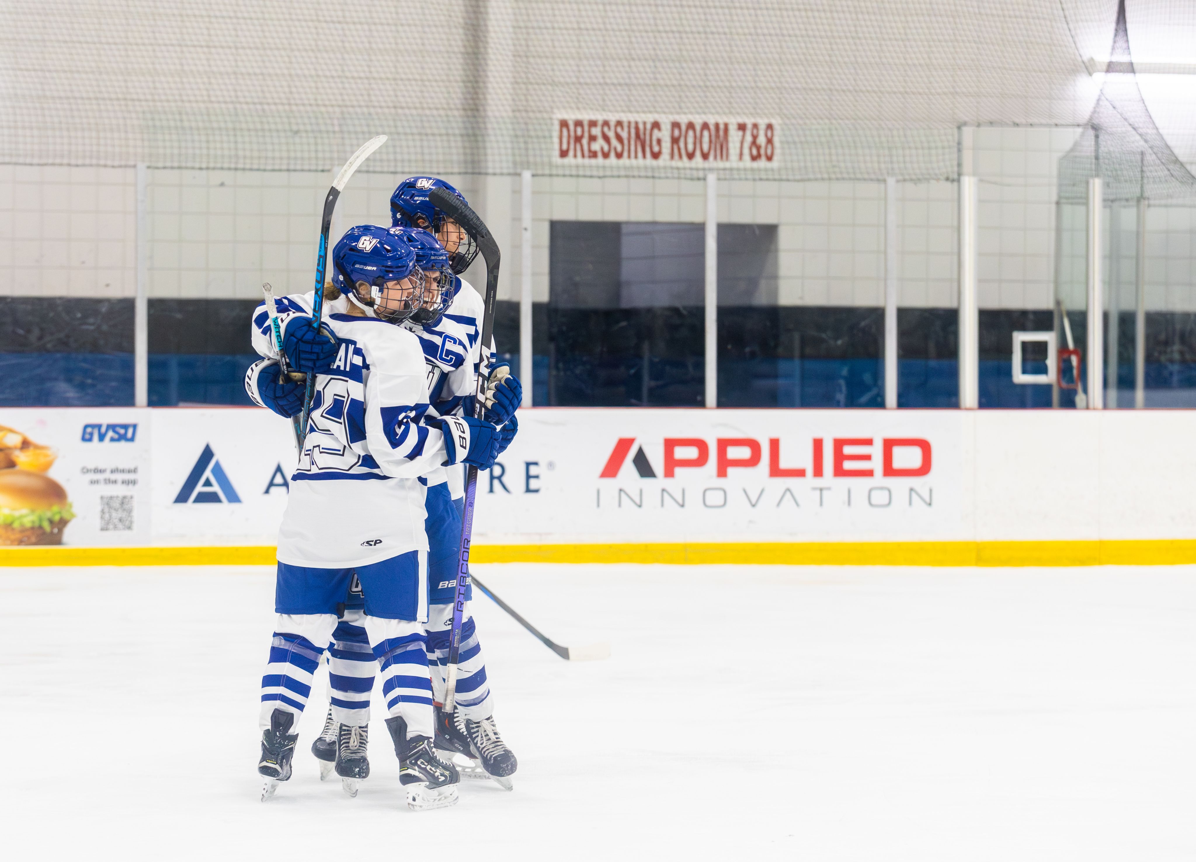 Three individuals in hockey gear hug each other on an ice rink.