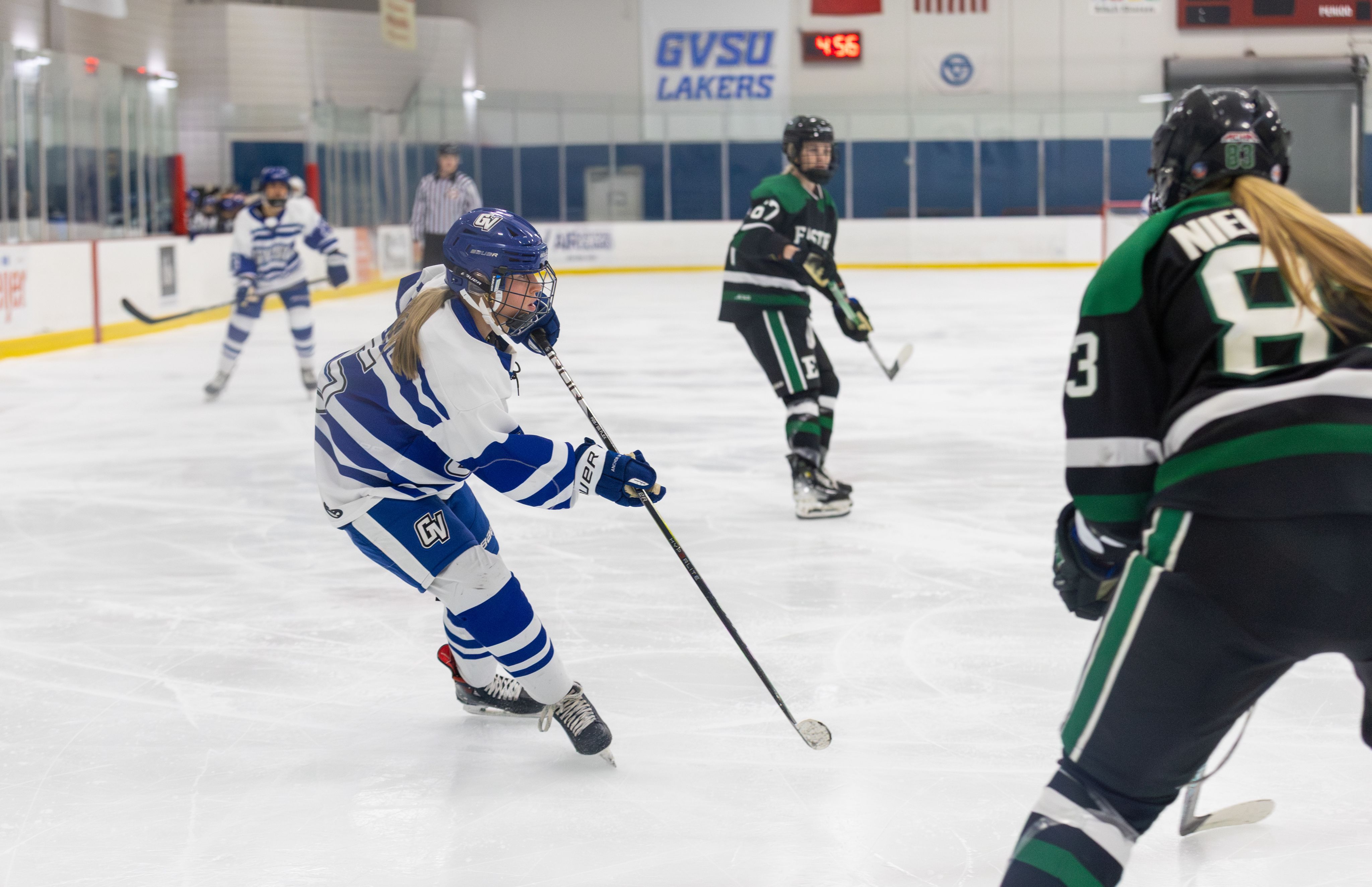 A hockey player leans with stick in hand while skating in an ice rink.