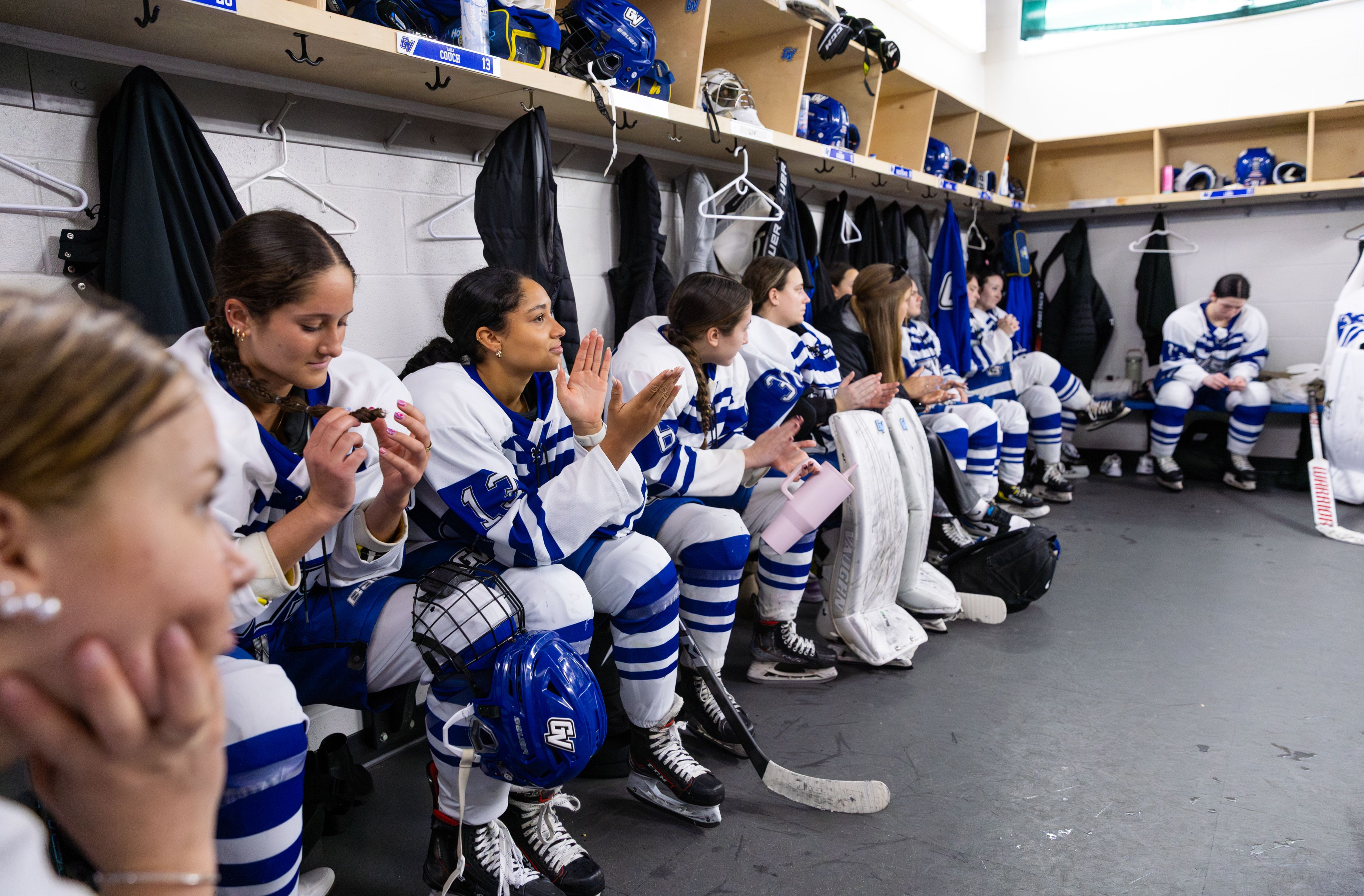 A group of hockey players sit on a locker room bench.
