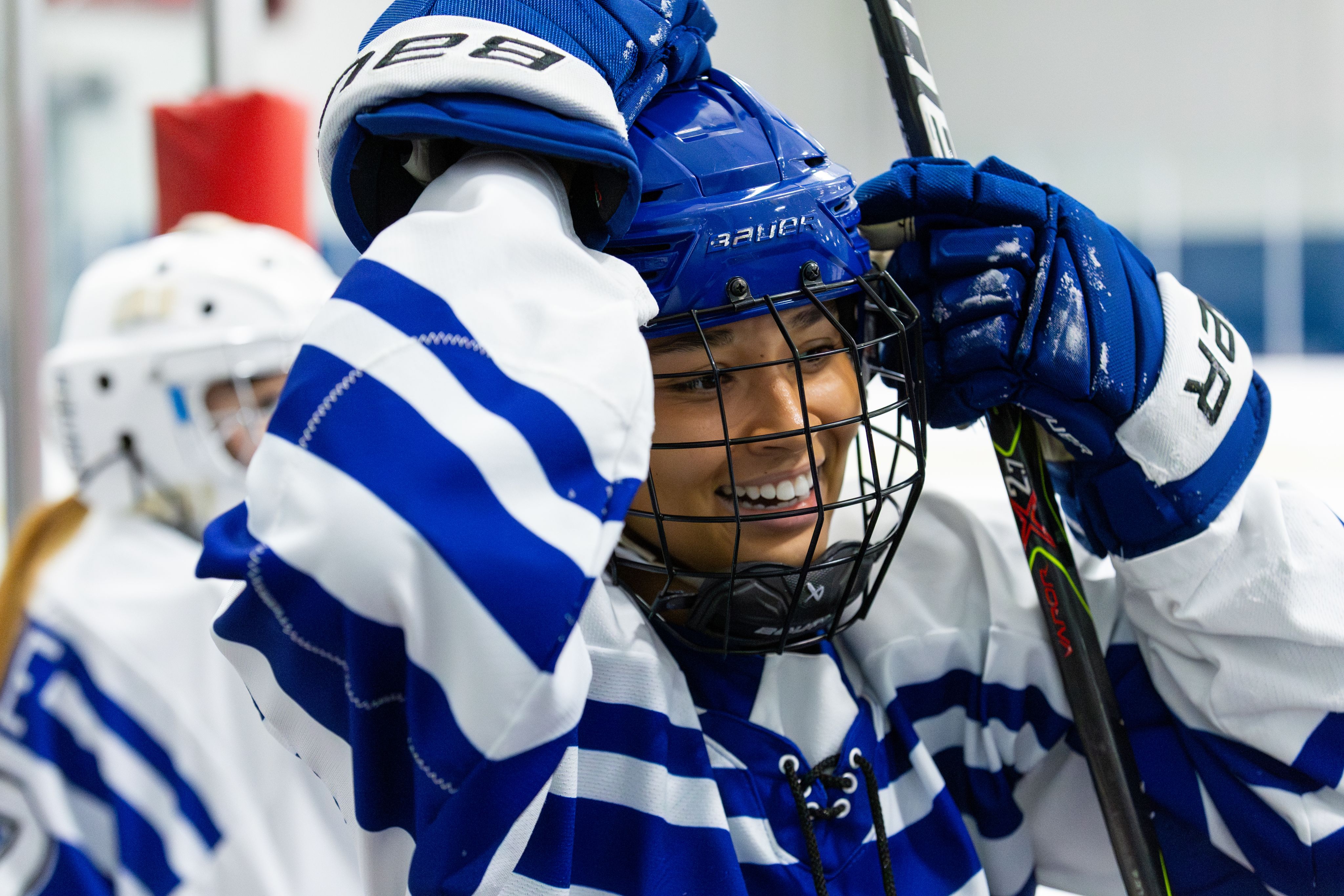A close up of a hockey player smiling while adjusting their helmet.