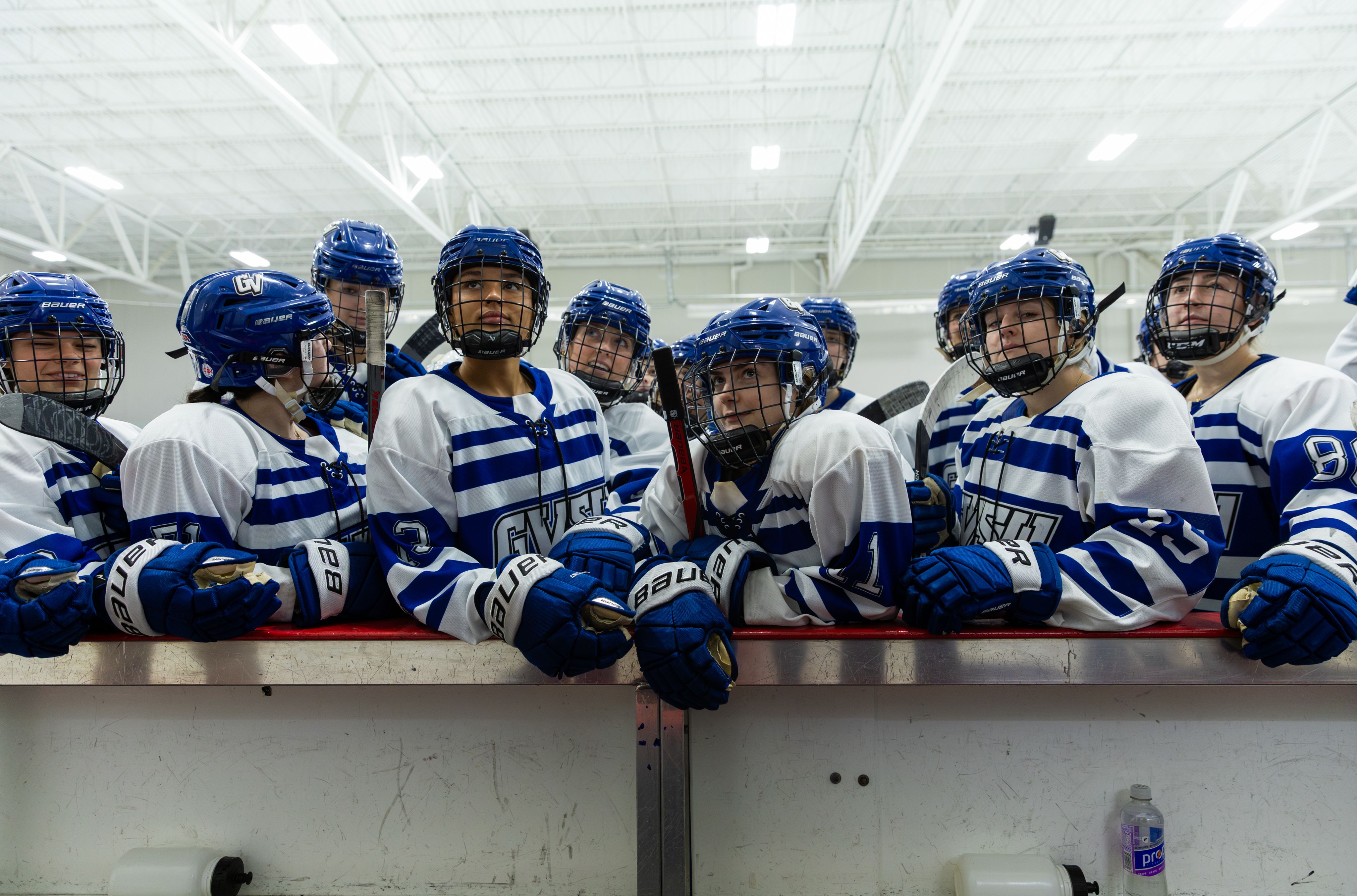 A hockey team stands at the edge of the rink looking onwards.