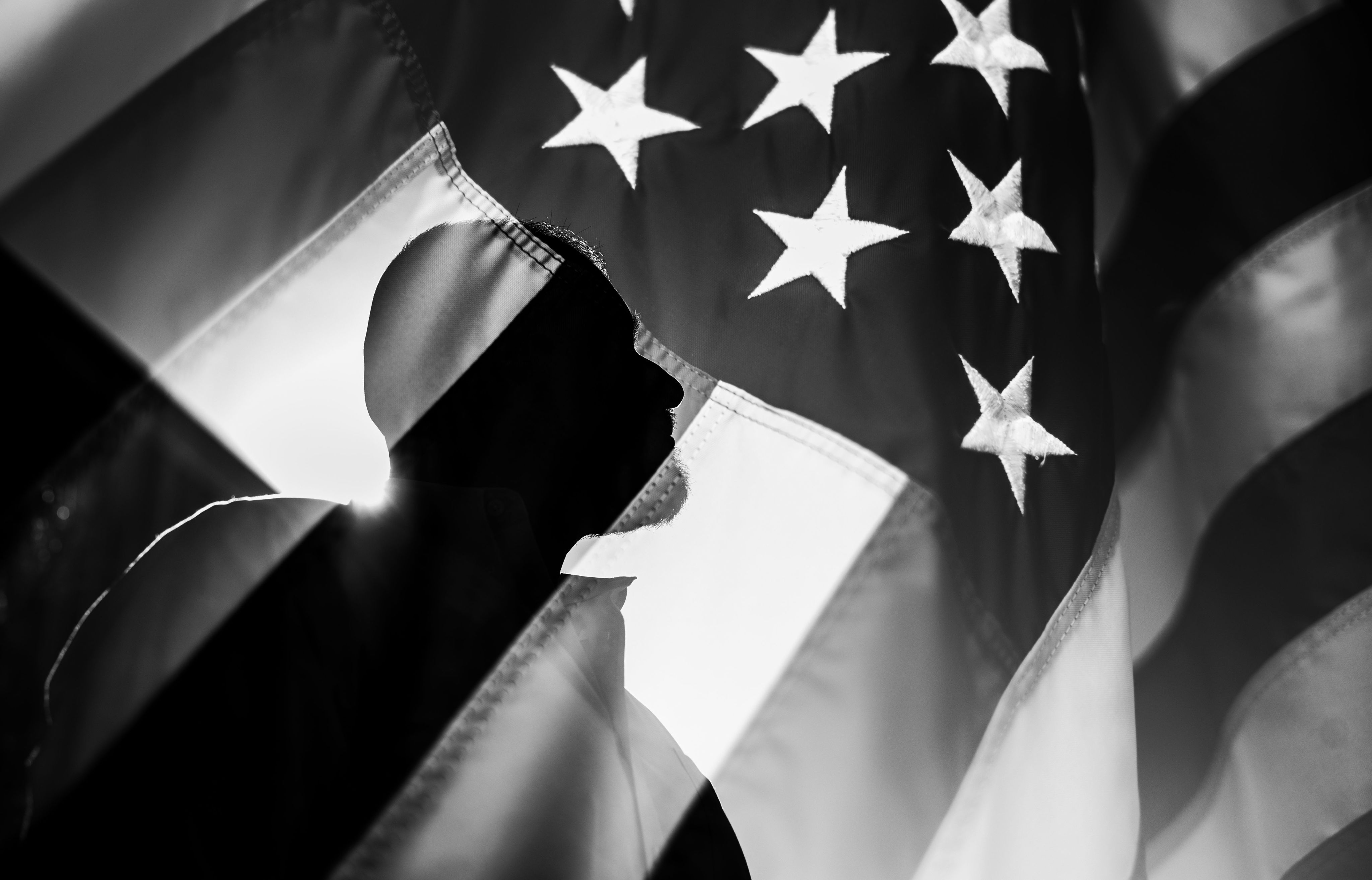 Silhouette of a person standing behind an American flag. (Photo by Kendra Stanley-Mills)