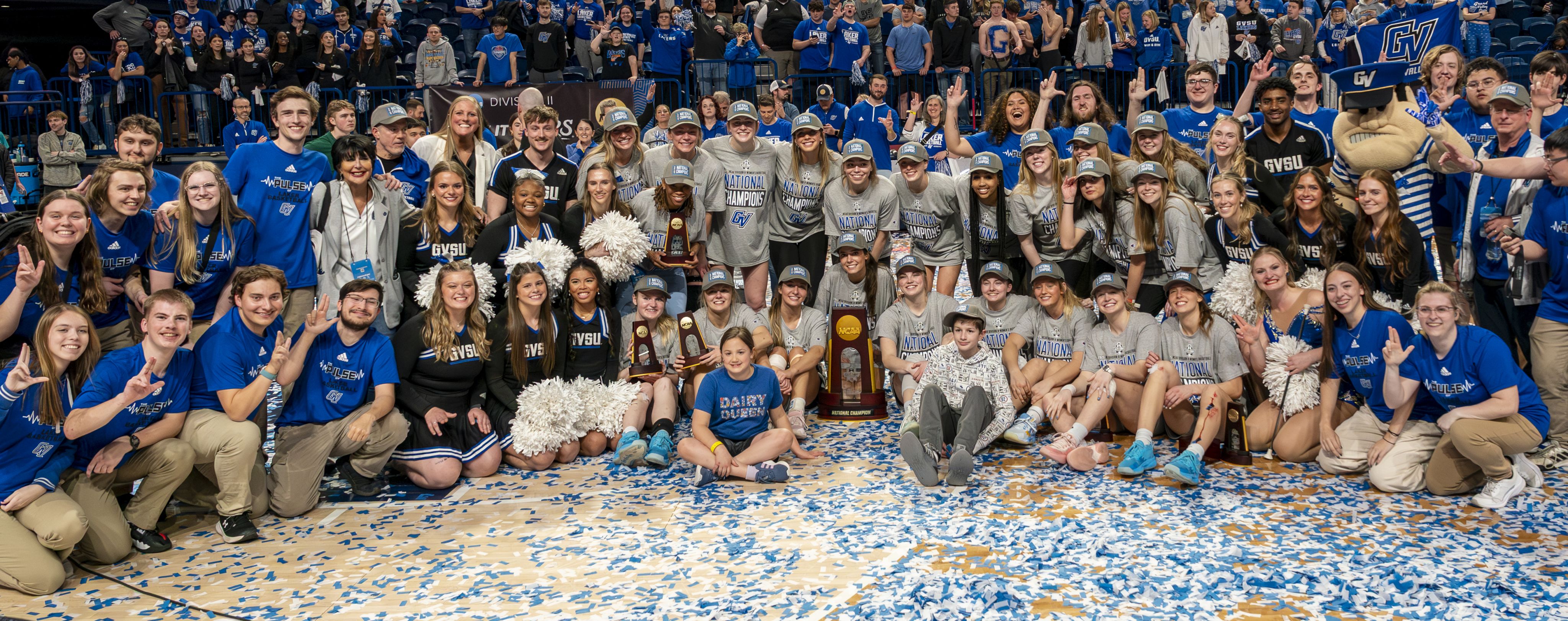 Grand Valley State University athletes, cheerleaders, staff, and fans celebrating on a basketball court after winning a championship, surrounded by blue and white confetti.