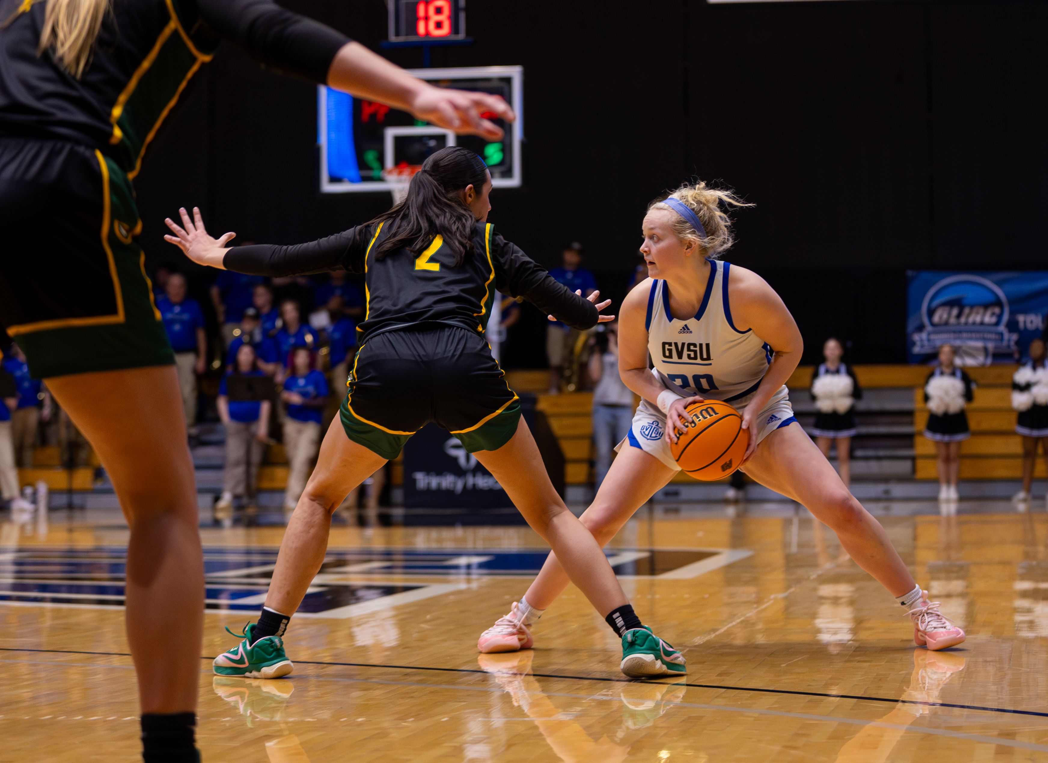 A Grand Valley basketball player holds the ball, guarded closely by a Wayne State player, looking for an opportunity to advance during the game.