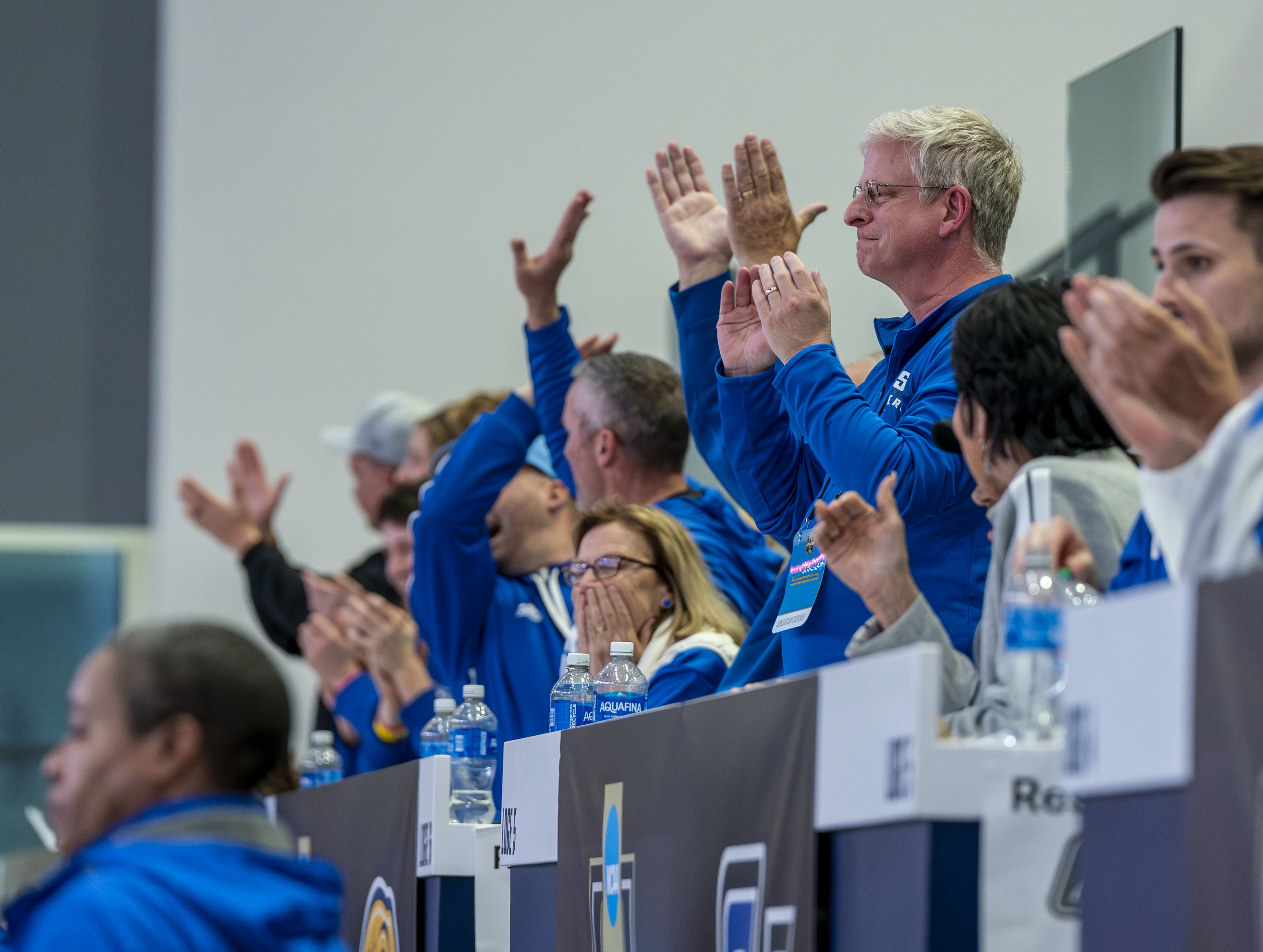 Fans standing and clapping enthusiastically in the stands at a basketball game, showing support for their team.