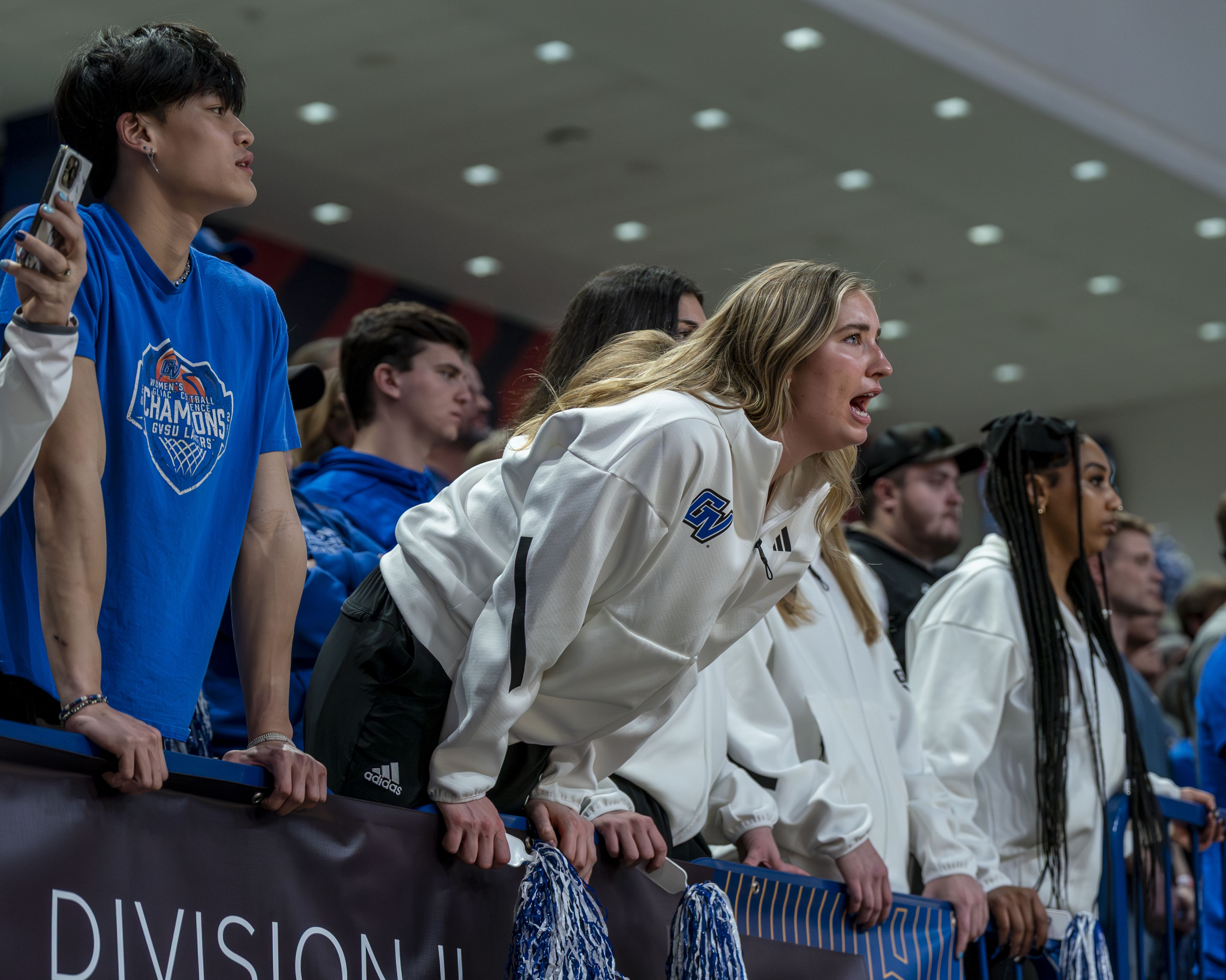 A Grand Valley fan leaning forward, intently cheering and supporting the team during a basketball game.