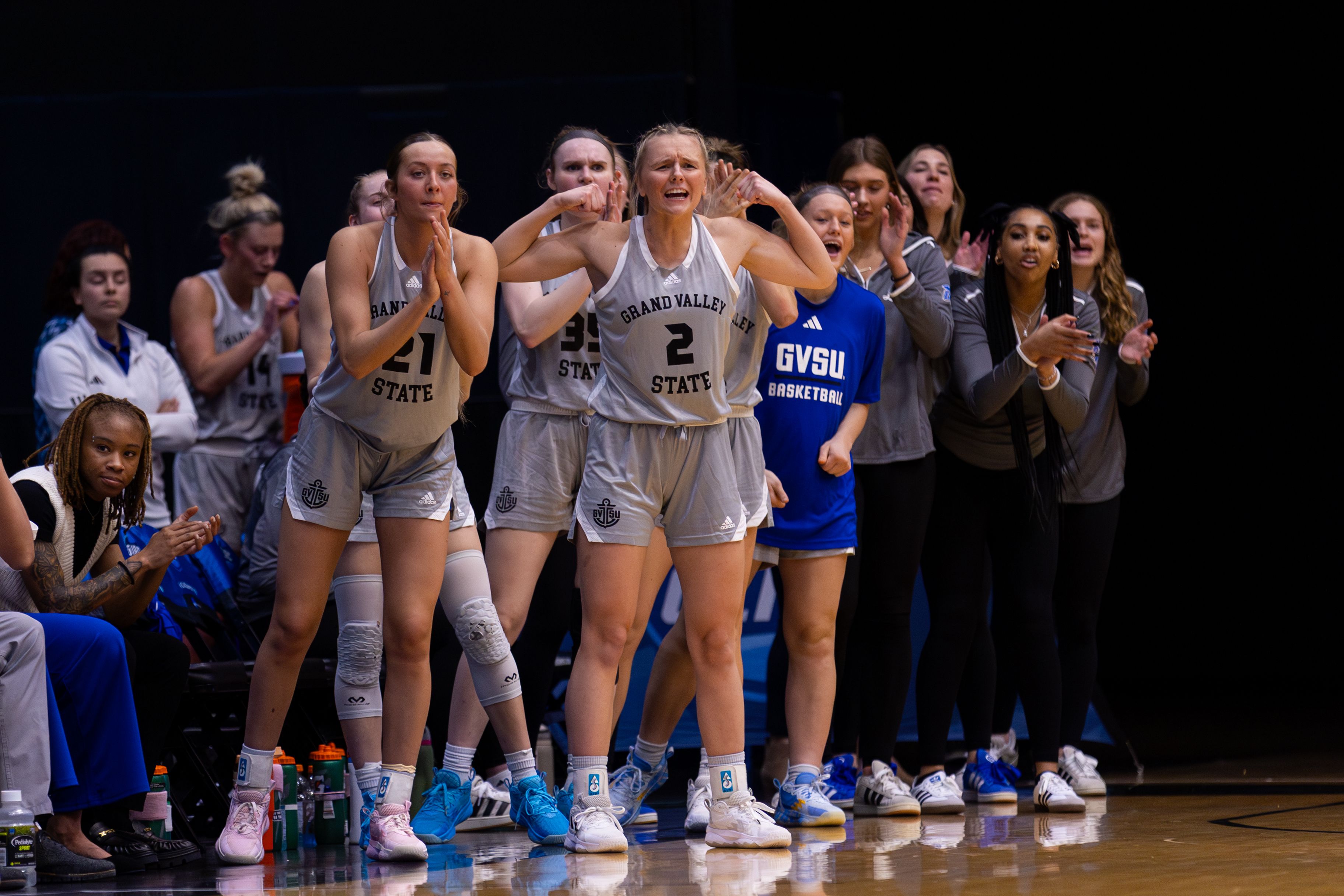Grand Valley basketball players standing and enthusiastically cheering from the sidelines during a game, expressing excitement and encouragement.