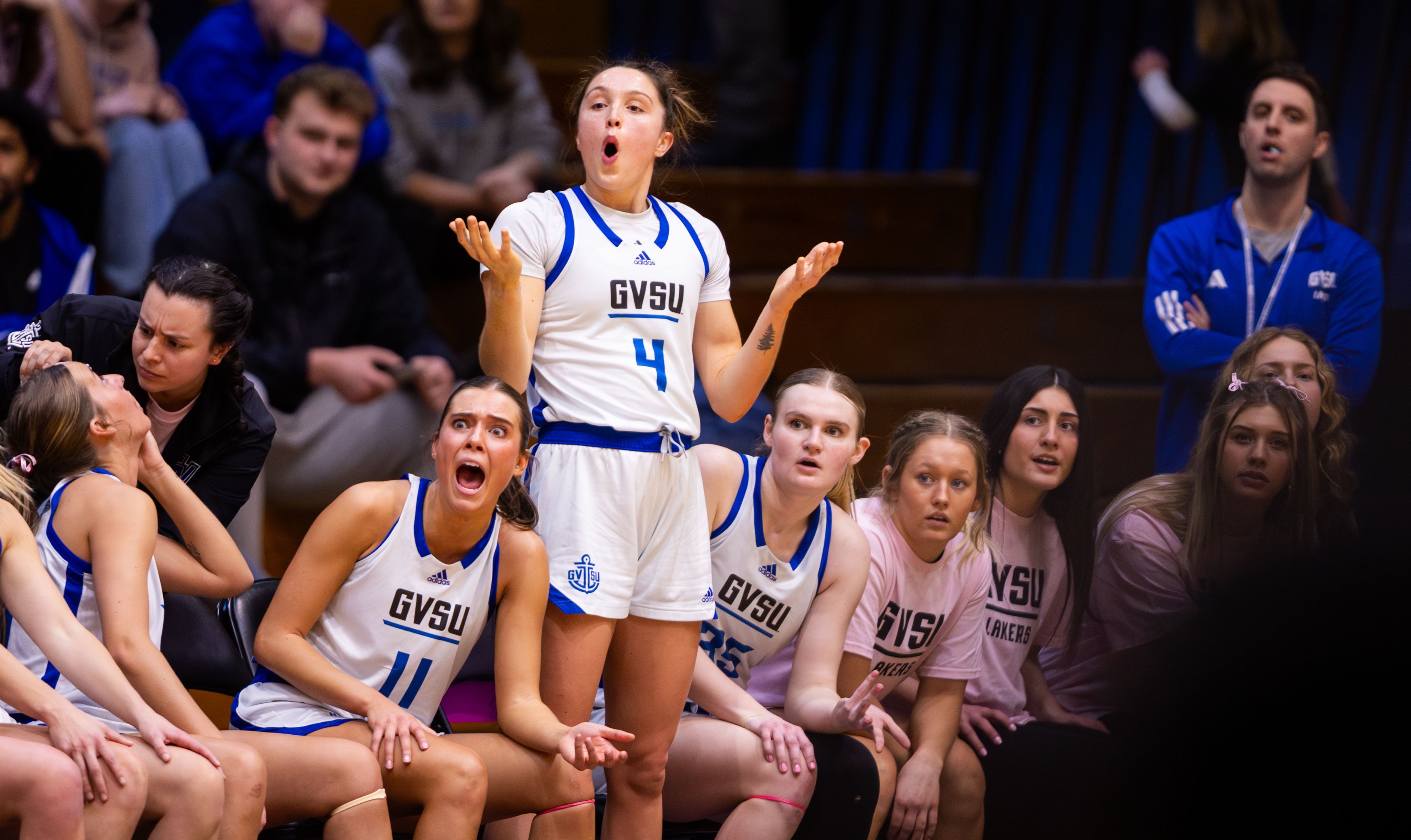 Grand Valley basketball players on the bench reacting dramatically to a call made, showing surprise, shock, and disbelief.