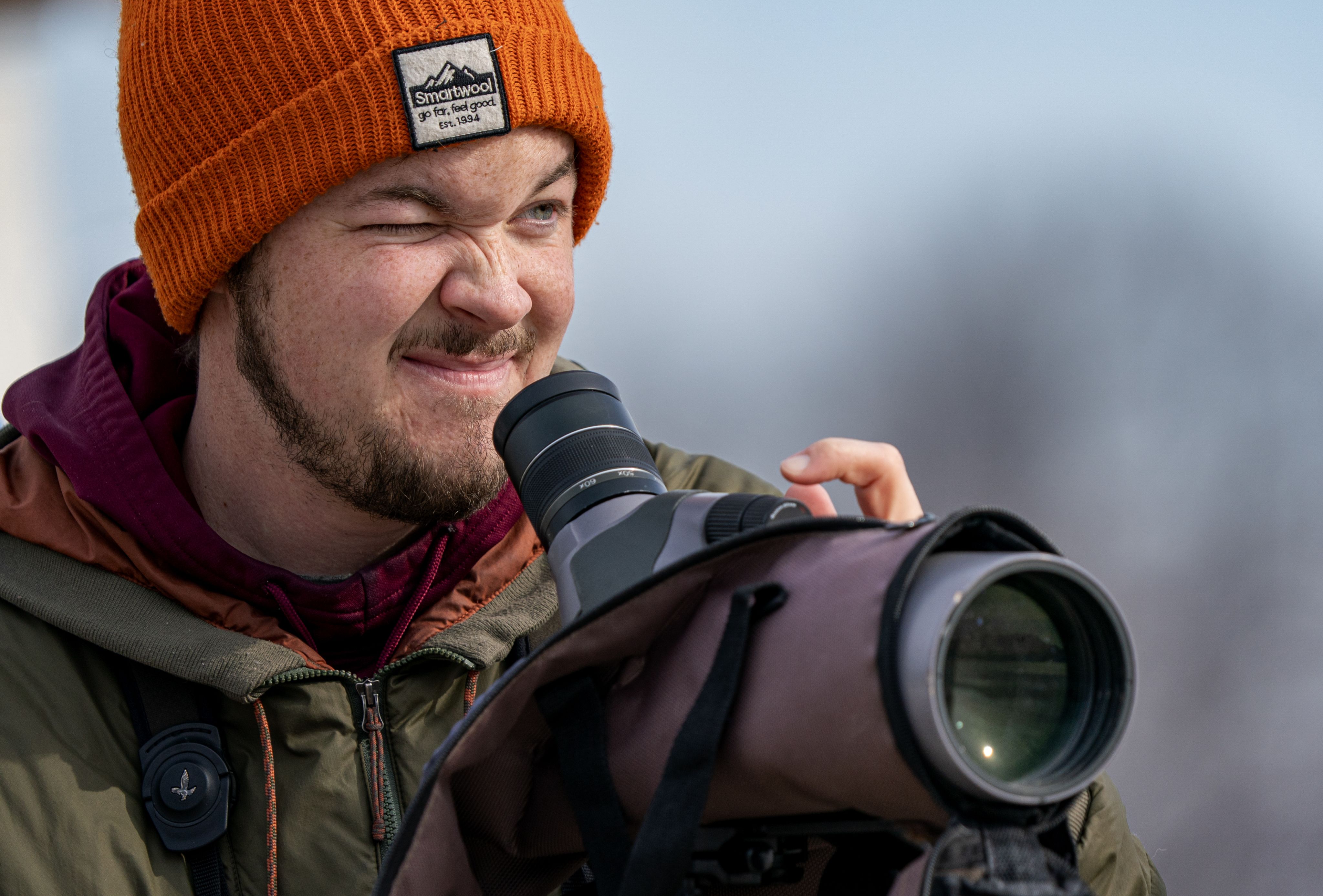 An individual squints one eye behind a spotting scope.