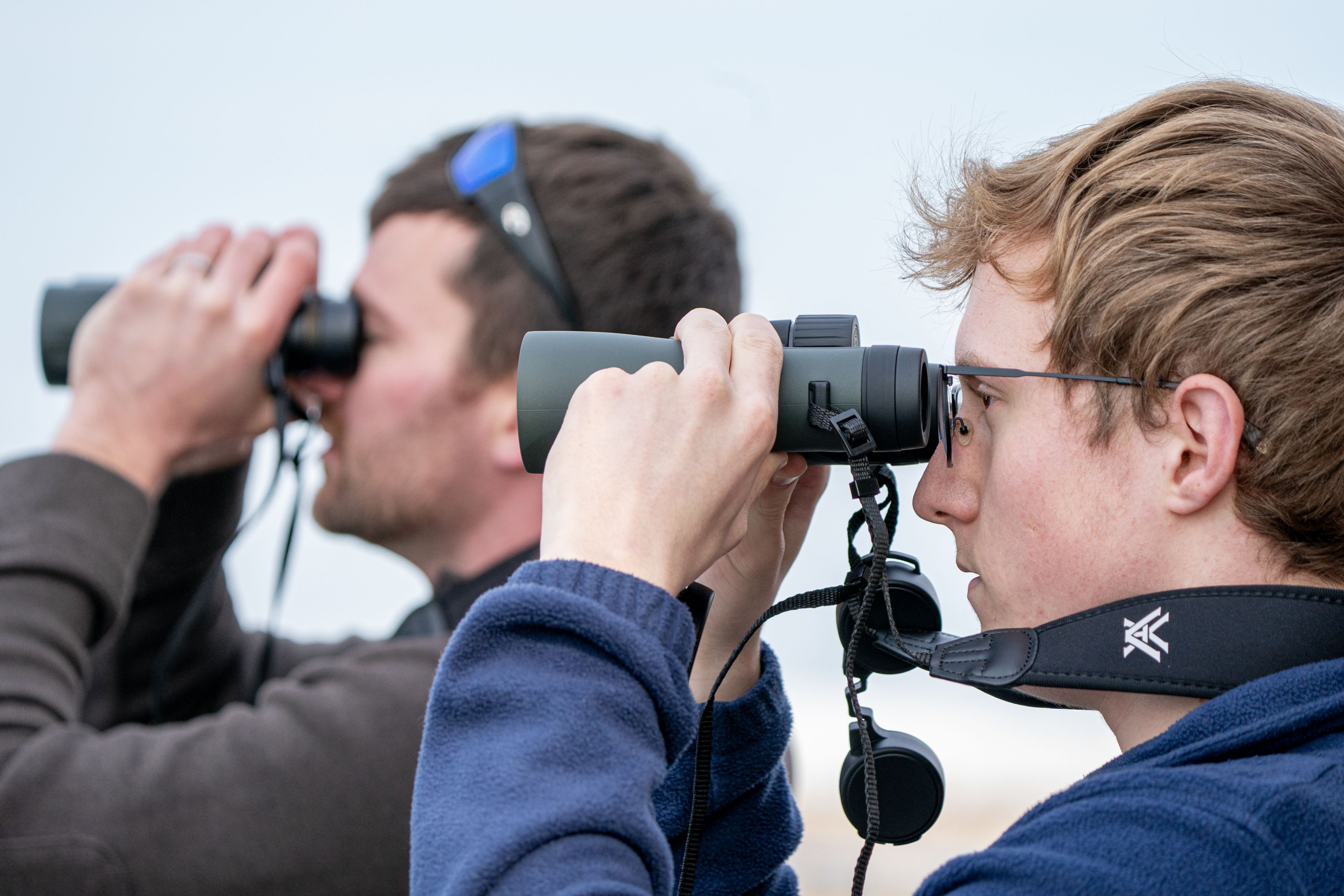 A close-up of two individuals looking through binoculars. 