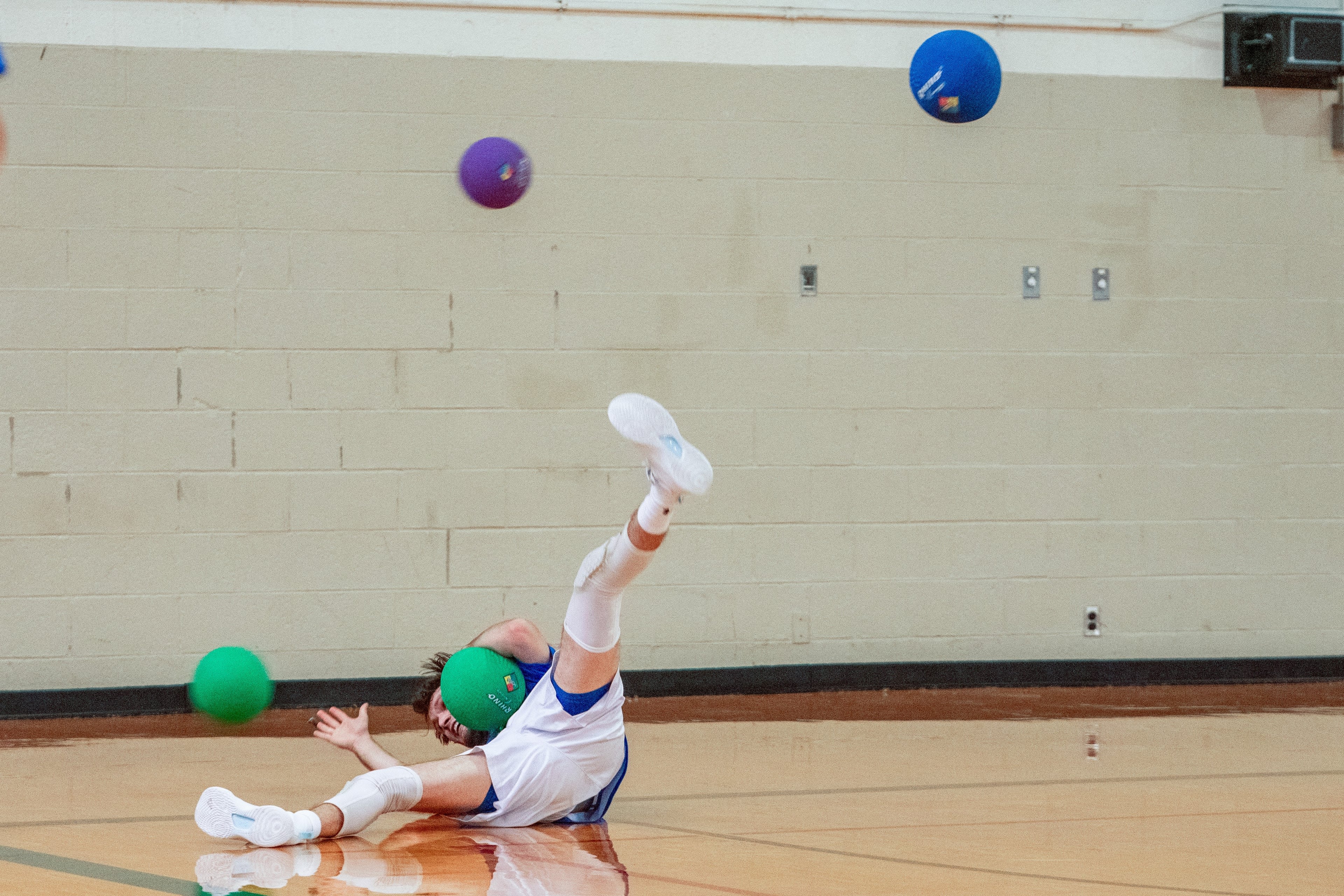 A player falls onto the ground clutching a dodgeball while other dodgeballs fly in the air.