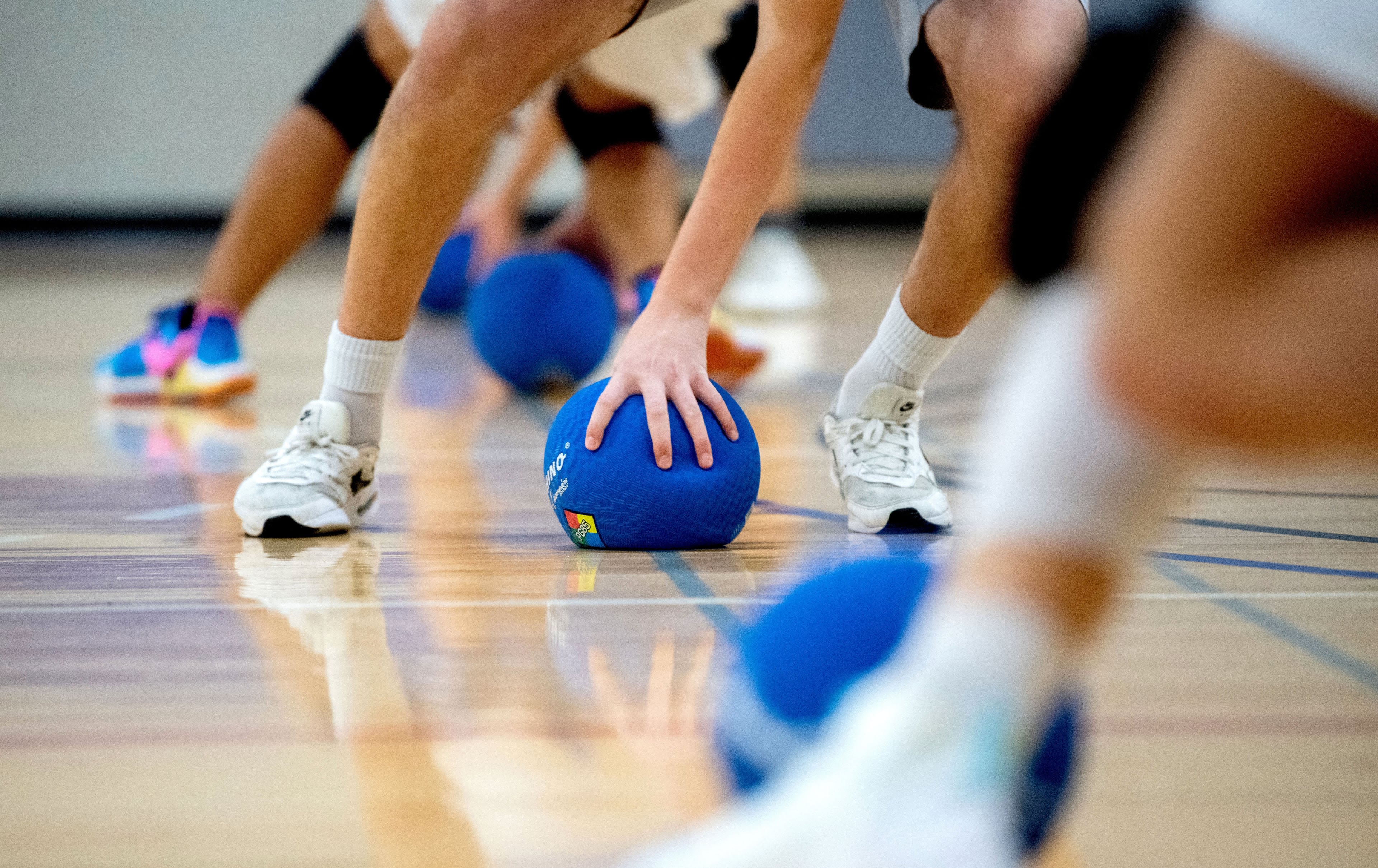 A close-up view of someone grabbing a dodgeball off the gym floor.