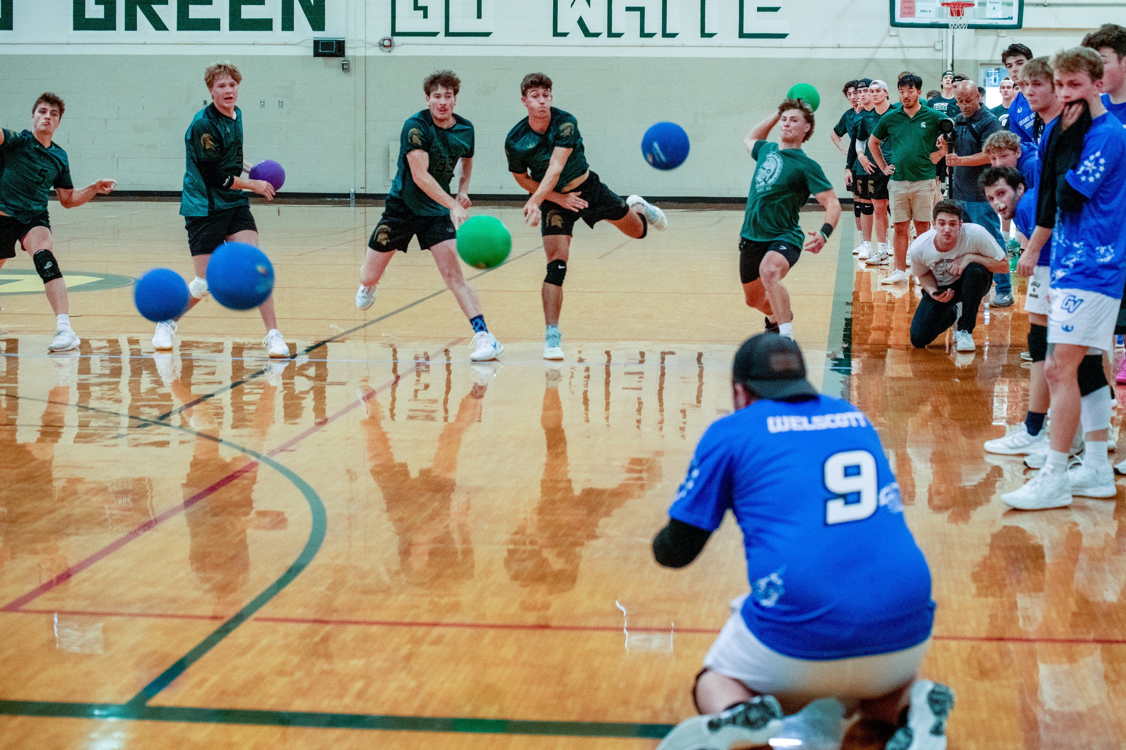 Multiple players throw dodgeballs at another player on their knees guarding themselves.