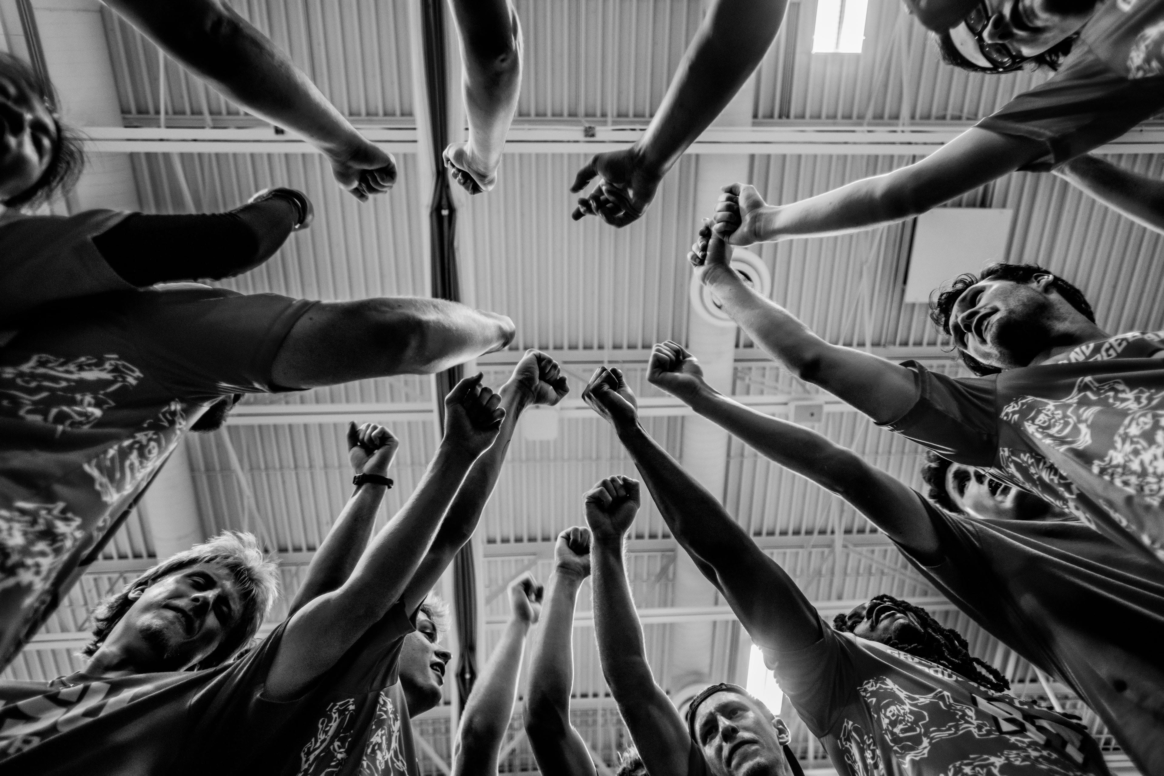 A black and white image from below a circle of players holding up fists as a team.