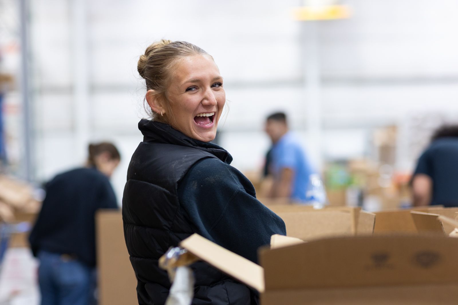 Sophia Shaw, a senior in Public and Nonprofit Administration flashes a smile while sorting boxes in a warehouse.