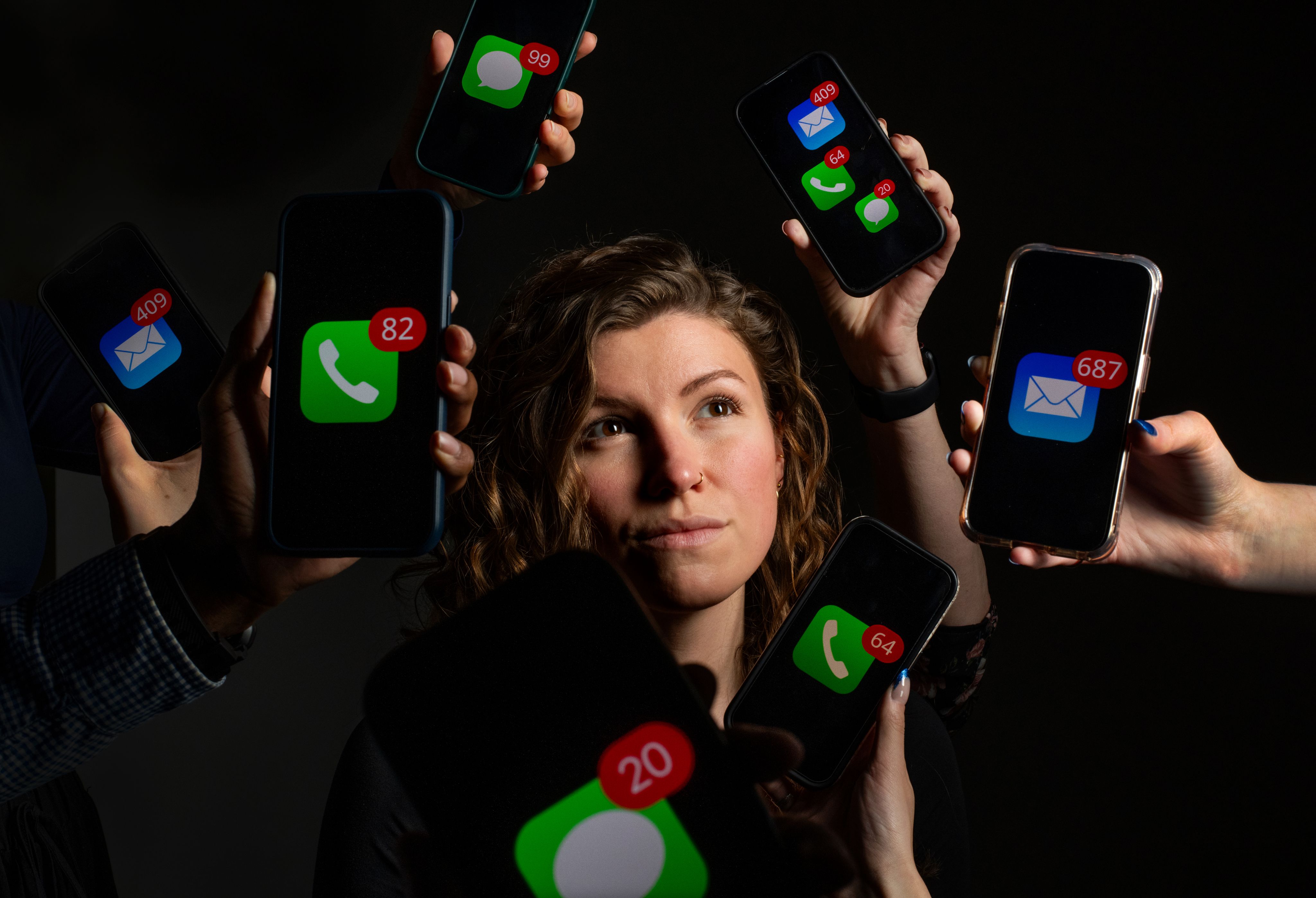 Abigail Austin poses for a portrait while smartphones indicating phone messages or emails are held around her face.