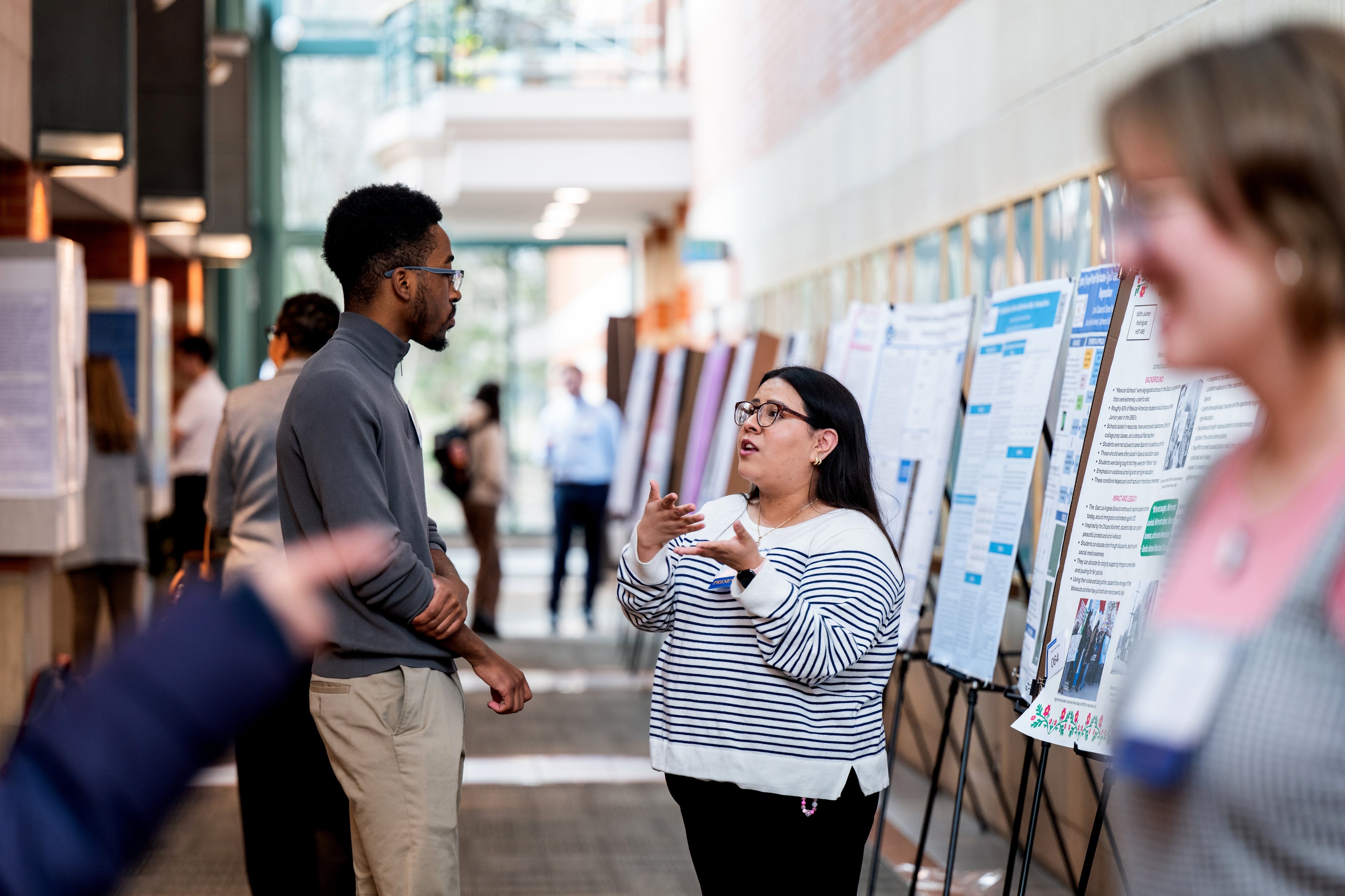 Senior secondary education in history first-generation student, Edith Juarez-Rodriguez, center, talks about her research with another Student Scholars Day presenter, John Chikwe, left, during poster presentations in Henry Hall April 8. Juarez-Rodriguez, a first-generation Mexican American, said her research is entitled “Understanding the Chicano Movement Through the Lens of Student Activism.”