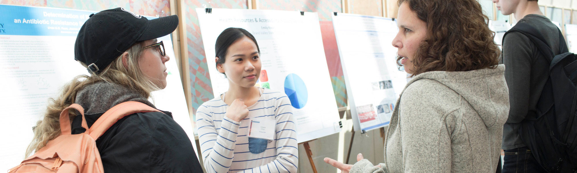 Students discuss a research poster being presented by another student.
