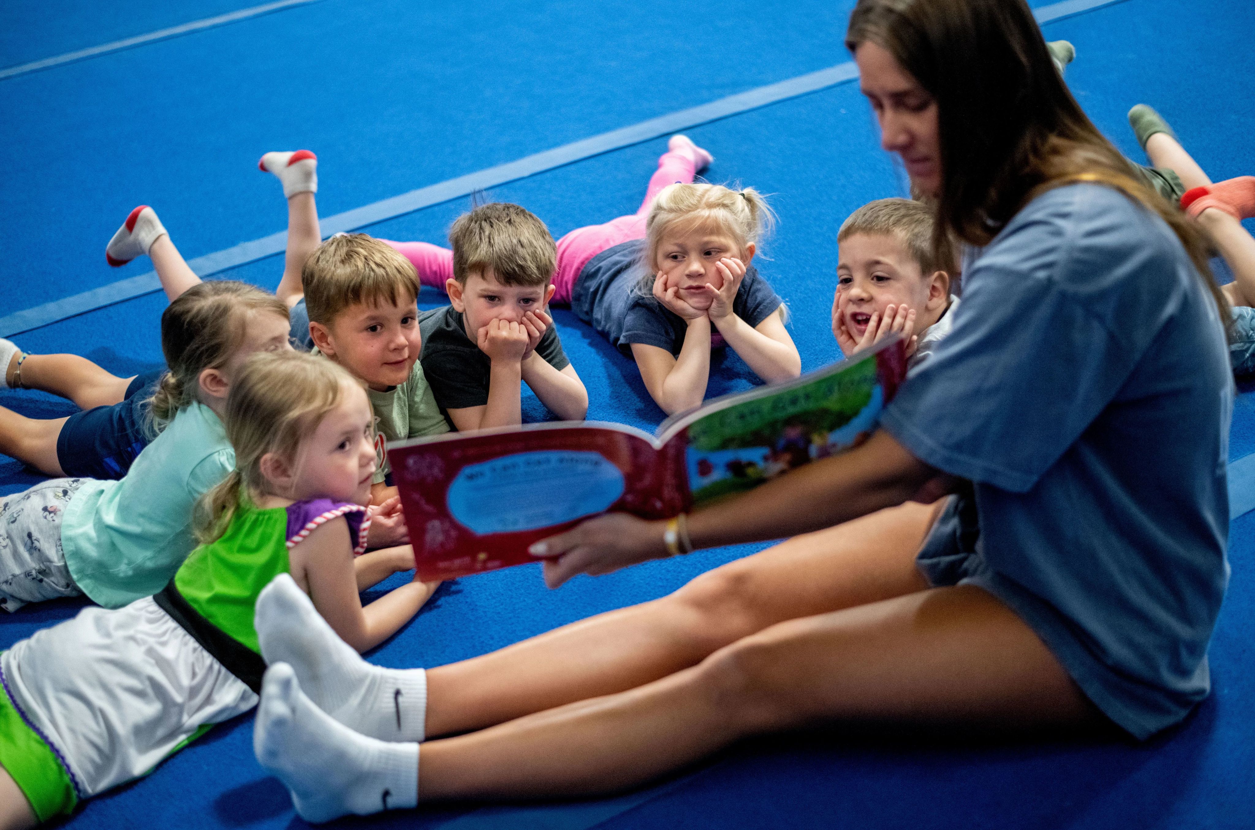 group of 6 preschoolers lying on the floor with their chins propped up in their hands as they listen to a student teacher read to them