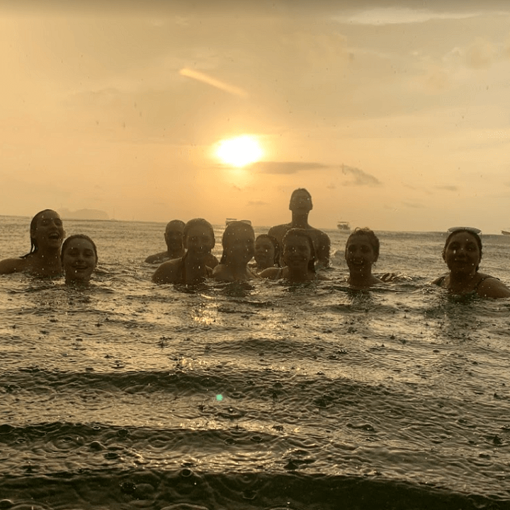 Image 1 of 8 Students swim in the rain at sunset.